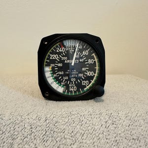 May include: A black airspeed indicator with a circular gauge and a needle pointing to 140 MPH. The gauge has white and green markings, with numbers from 40 to 240. The instrument also displays temperature in Celsius.