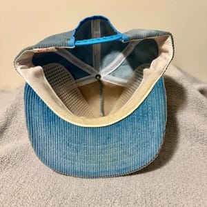 Op de afbeelding: Blauwe corduroy baseballcap met een gebogen klep en een blauwe verstelbare band. De binnenkant heeft een witte mesh voering en een zweetband. De pet heeft een vintage, versleten uitstraling.