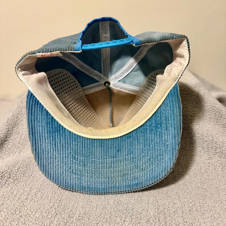 Op de afbeelding: Blauwe corduroy baseballcap met een gebogen klep en een blauwe verstelbare band. De binnenkant heeft een witte mesh voering en een zweetband. De pet heeft een vintage, versleten uitstraling.