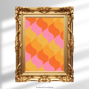 May include: A framed cross-stitch artwork with a retro design. The artwork features a repeating pattern of wavy shapes in shades of pink, orange, and yellow. The frame is ornate and gold-coloured, adding a vintage aesthetic. The text "AestheticCrossStitch" is at the bottom.