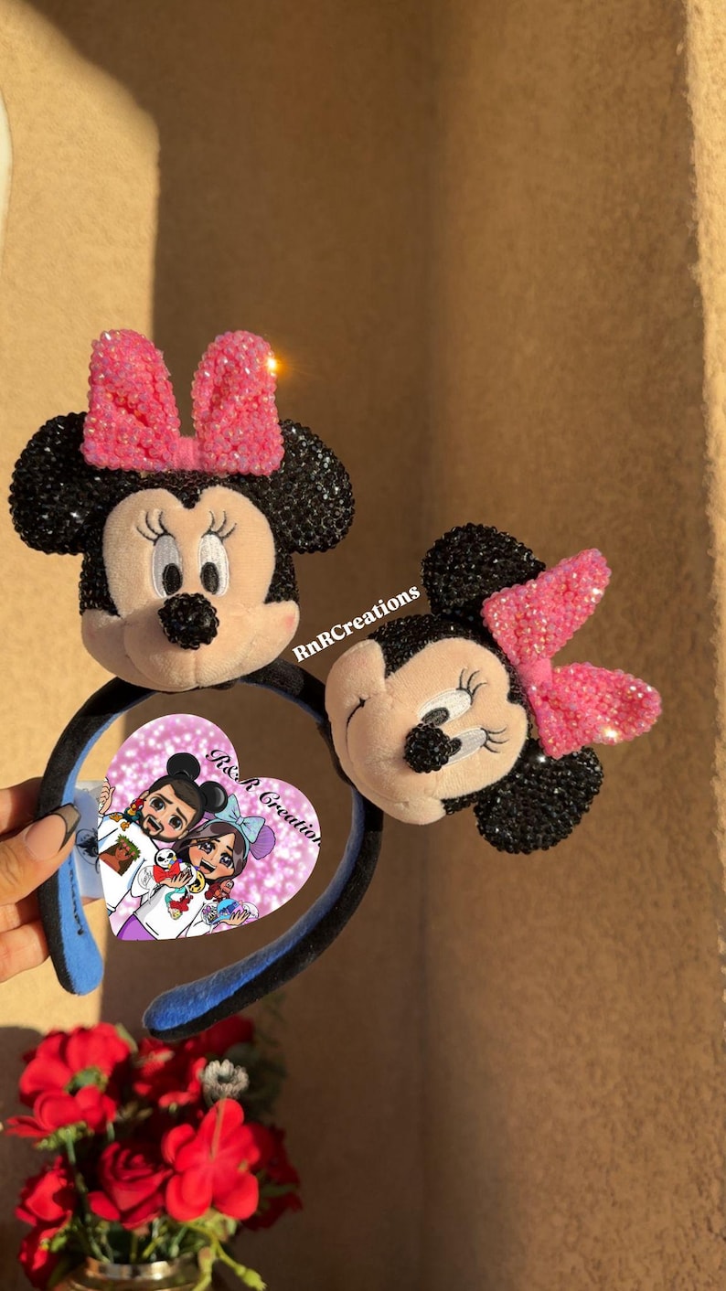 May include: Two Minnie Mouse ear headbands. One features a full Minnie Mouse face with a pink sequined bow. The other headband has a Minnie Mouse face with a pink sequined bow. The headband has a black band with blue accents. The image has the text "RnR Creations" and a heart-shaped image.