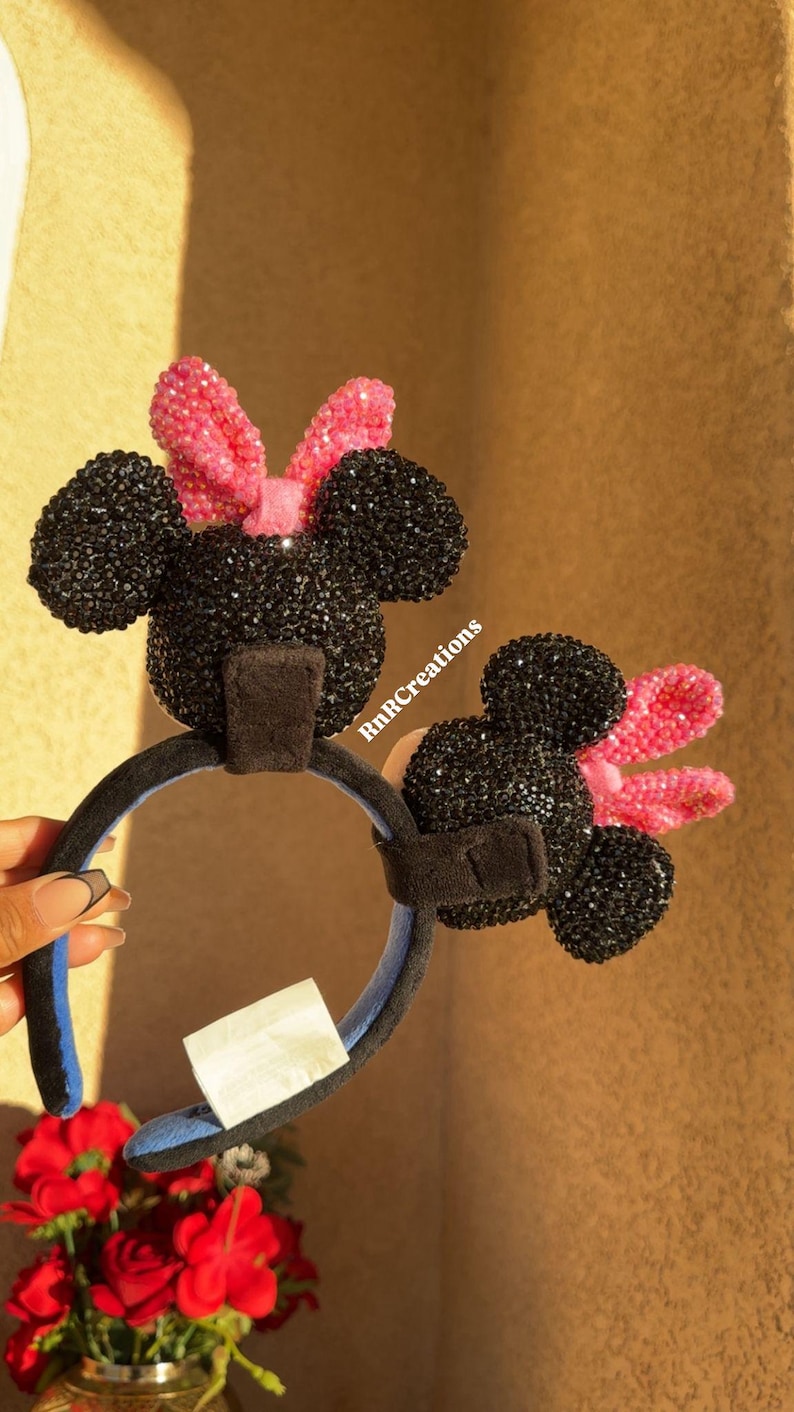 May include: Black and pink Minnie Mouse ear headbands. The ears are covered in black rhinestones, and the bows are pink. The headband is black with a blue interior. The text "RnRcreations" is visible.