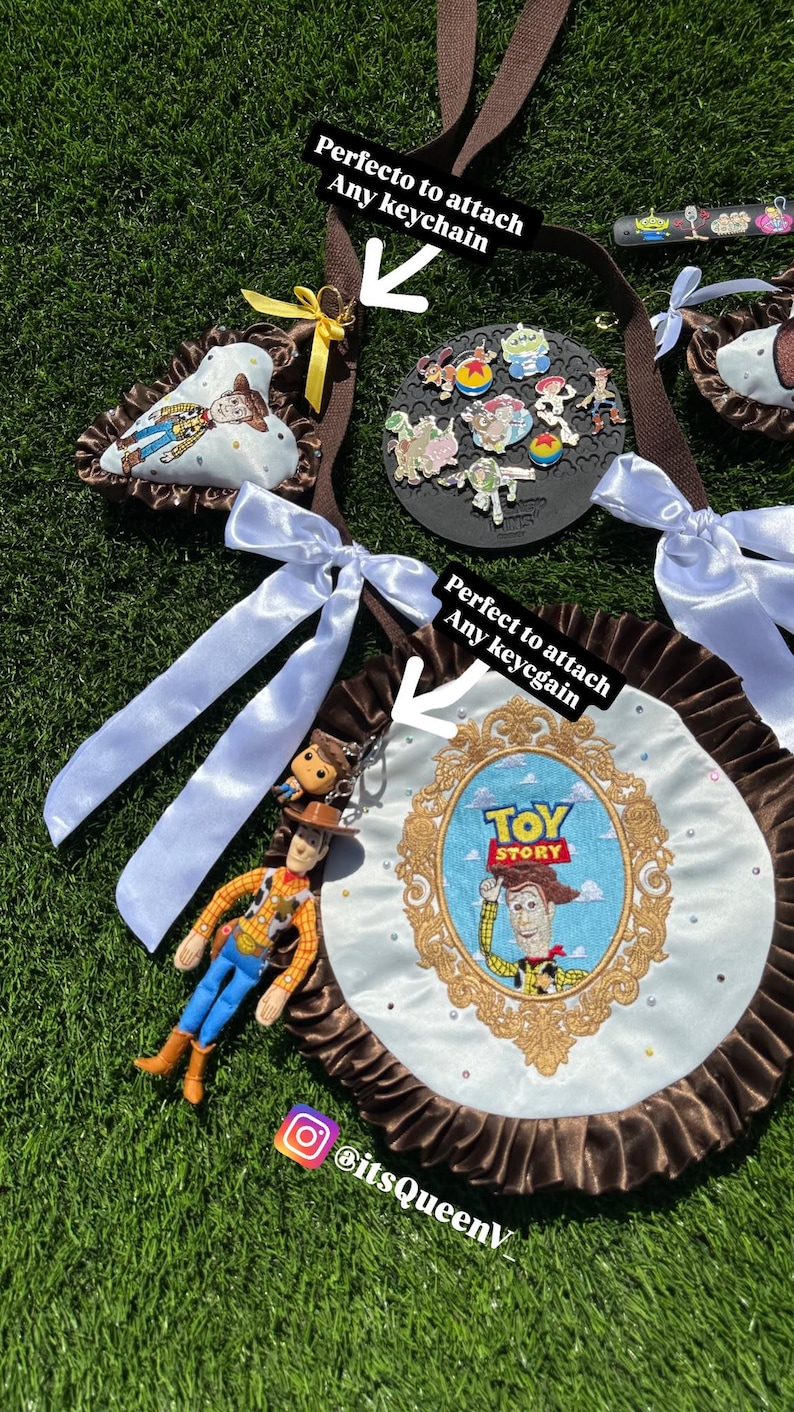May include: A brown fabric strap featuring a round white satin display board with a gold embroidered Toy Story frame and Woody character. The board has a brown ruffled edge, white satin bows, and a hanging Woody figurine keychain attached.