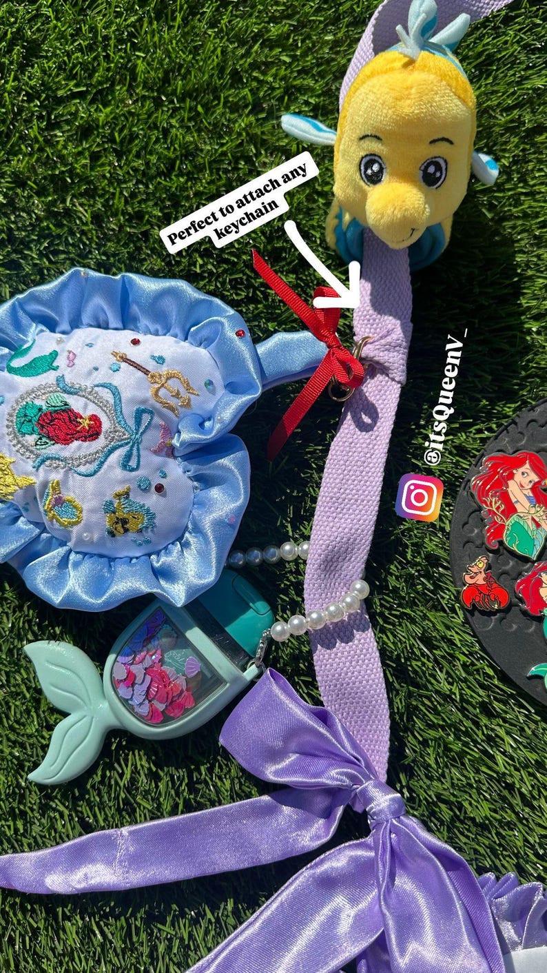 Op de afbeelding: Een verzameling accessoires met het thema De Kleine Zeemeermin, waaronder een pluche Botje, een blauw-wit geborduurd zakje, een handdesinfectiehouder in de vorm van een zeemeerminstaart en een paarse lanyard met een strik.
