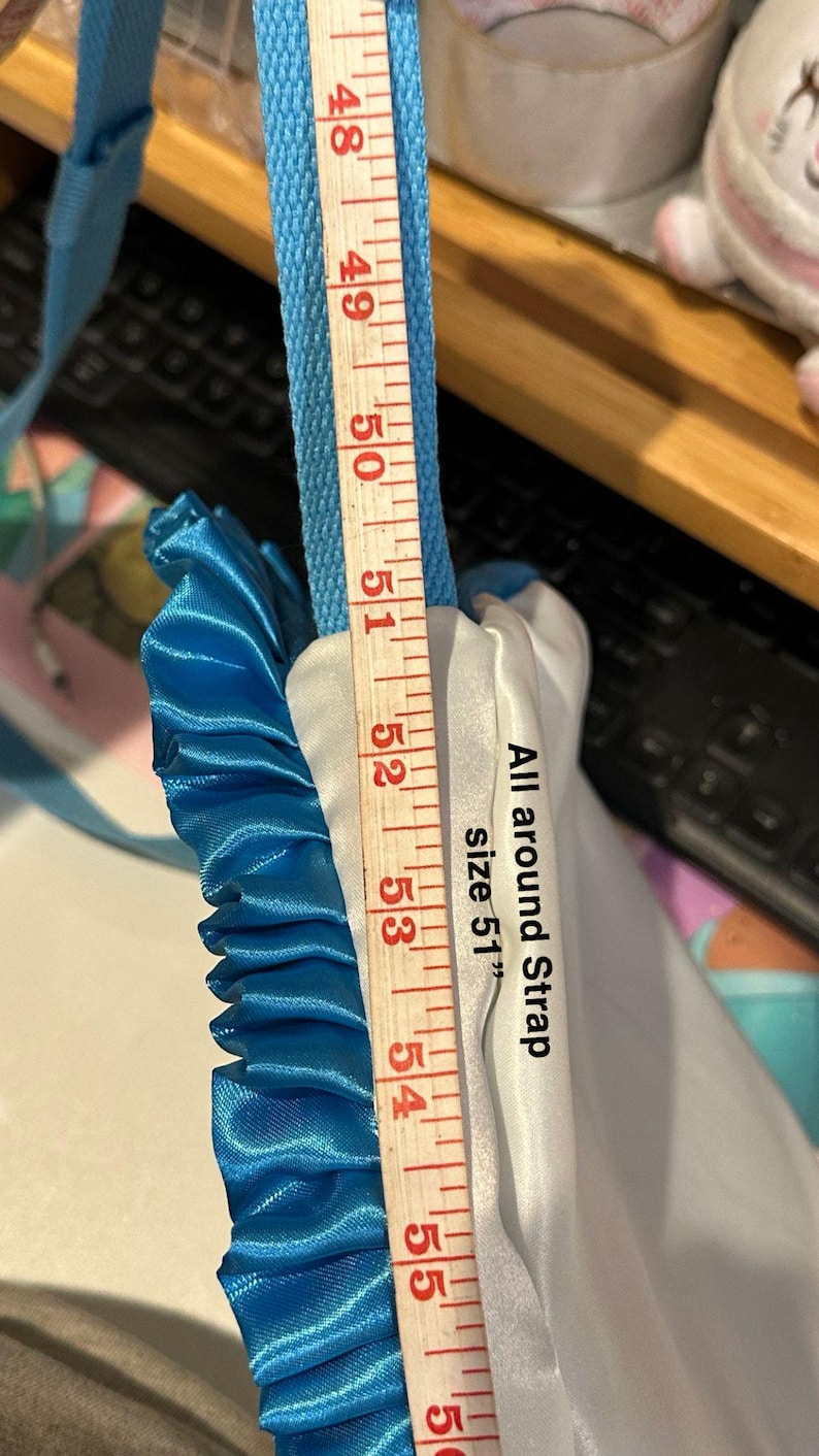 Op de afbeelding: Een blauw en wit stoffen item met een blauwe band, gemeten met een houten liniaal. De tekst op het item luidt "All around Strap size 51". De liniaal toont een meting van 129.5 cm.
