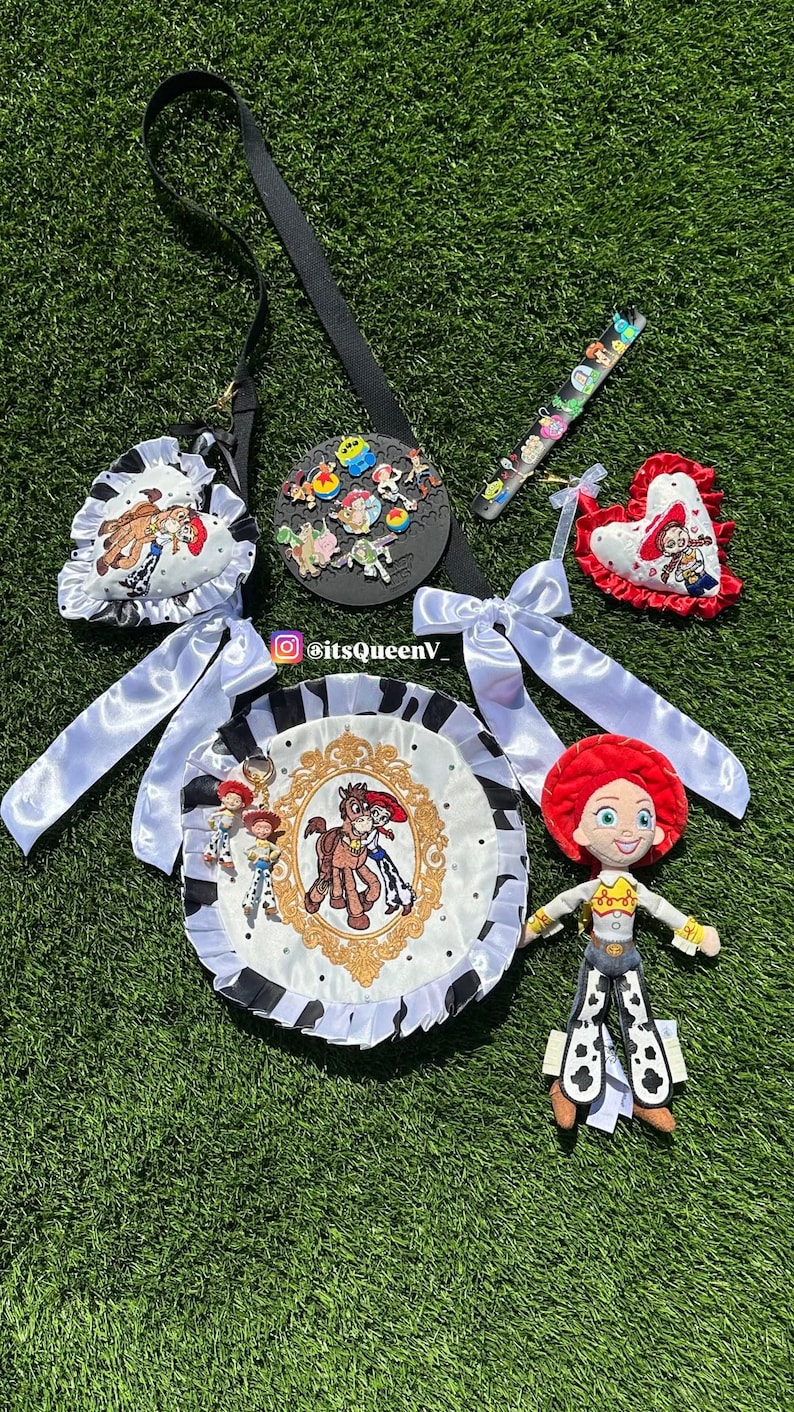 May include: A collection of Toy Story themed accessories including a round bag with a black and white cow print ruffle, a heart-shaped pin display, a plush Jessie doll, and various character pins. The bag features a gold frame graphic with Jessie and Bullseye. Text reads itsQueenV_.