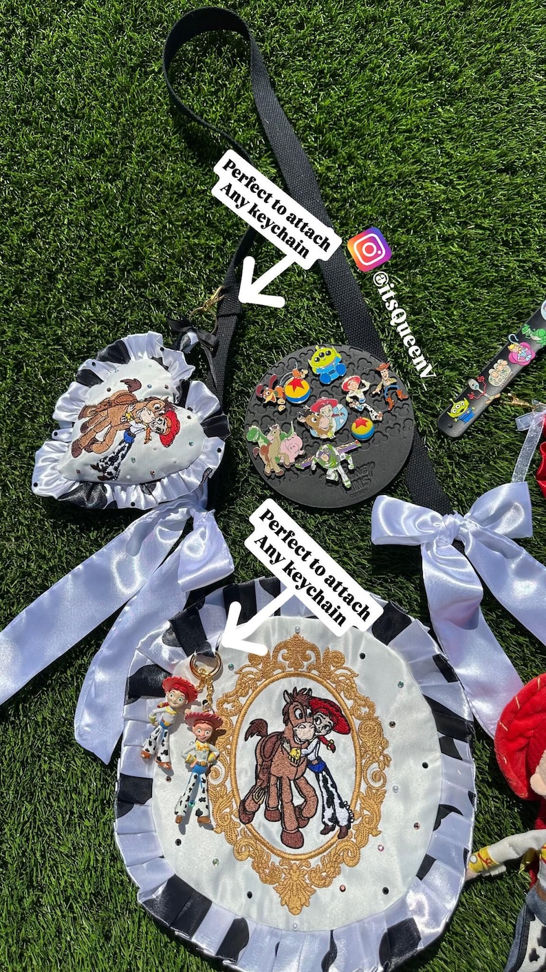 May include: A black strap with two white satin bows and two circular fabric badges featuring Toy Story character embroidery, gold-tone frames, and rhinestones. The badges have text reading Perfect to attach Any keychain and @itsQueenv.
