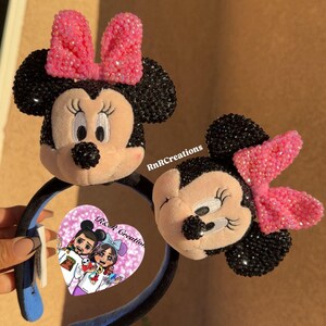 May include: Two Minnie Mouse ear headbands. One headband is held by a hand. The ears are black with pink bows. The Minnie Mouse faces are beige with black noses and eyelashes. The headband is black with blue accents. The image has the text "RnR Creations".