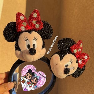 May include: Two Minnie Mouse ear headbands. The ears are black with red bows adorned with rhinestones. The headband has a black band with a blue interior. One headband has a heart-shaped tag with a cartoon couple.