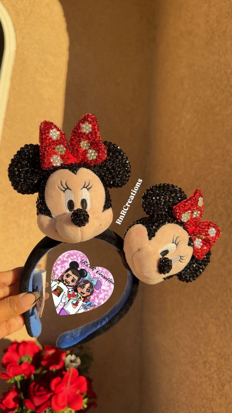 May include: Two Minnie Mouse ear headbands. The ears are black with red bows adorned with rhinestones. The headband has a black band with a blue interior. One headband has a heart-shaped tag with a cartoon couple.