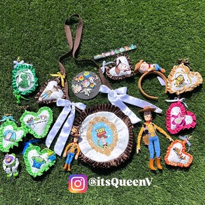 May include: A collection of Toy Story themed items including a round bag with a Woody graphic, several heart-shaped fabric ornaments with character prints, a Woody action figure, a headband, and a circular pin display with the text itsQueenV.