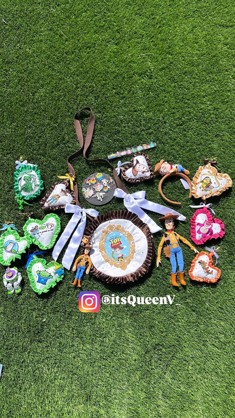 May include: A collection of Toy Story themed items including a round bag with a Woody graphic, several heart-shaped fabric ornaments with character prints, a Woody action figure, a headband, and a circular pin display with the text itsQueenV.