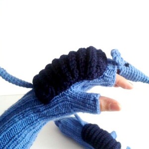 Op de afbeelding: Blauwe en zwarte gebreide vingerloze handschoenen met een armadillo-ontwerp. De armadillo heeft een lange staart en een puntige snuit.