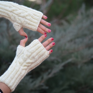 May include: A pair of white knitted fingerless gloves with a cable knit pattern. The gloves are made of a soft, warm yarn and are perfect for keeping your hands warm in the winter.