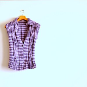 May include: A purple and white striped sleeveless knitted vest with a collar hanging on a wooden hanger.