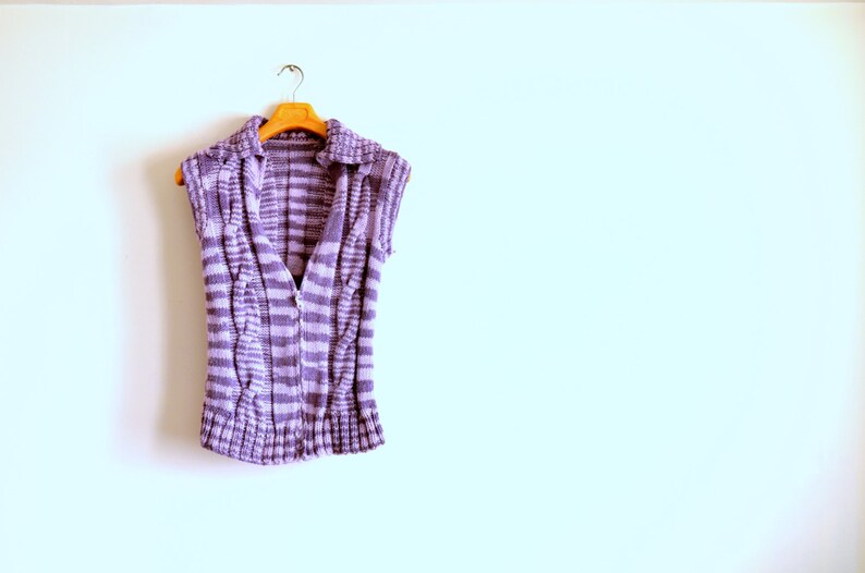 May include: A purple and white striped sleeveless knitted vest with a collar hanging on a wooden hanger.