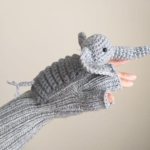 May include: Gray knitted fingerless gloves with a gray crocheted elephant puppet attached. The elephant has black eyes and a long trunk.