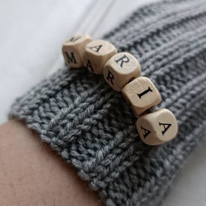 May include: A gray knitted glove with the name "MARIA" spelled out in wooden letter beads.