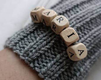Puede incluir: Un guante de punto gris con el nombre "MARIA" escrito en cuentas de letras de madera.