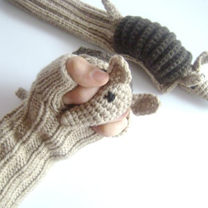May include: A pair of beige knitted fingerless gloves with a brown and beige crocheted armadillo attached to the cuff.