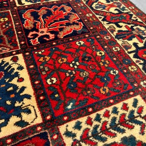 May include: Close-up of a rectangular, patterned rug with a repeating design. The rug features a cream-colored background with red, navy blue, and brown geometric shapes and floral motifs. The rug has a detailed border.