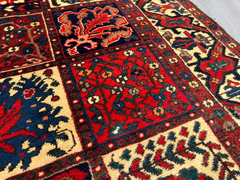 May include: Close-up of a rectangular, patterned rug with a repeating design. The rug features a cream-colored background with red, navy blue, and brown geometric shapes and floral motifs. The rug has a detailed border.