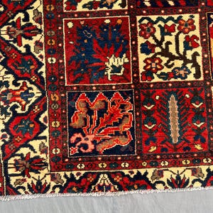 May include: Close-up of a section of a traditional rug with a repeating pattern. The rug features a cream-colored background with red, navy blue, and brown geometric and floral designs. The border is a dark red with intricate patterns.