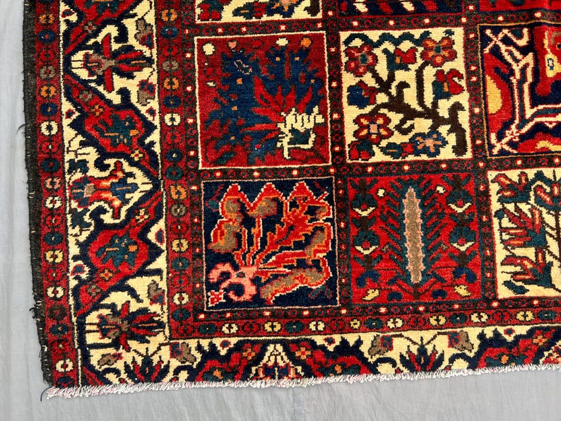 May include: Close-up of a section of a traditional rug with a repeating pattern. The rug features a cream-colored background with red, navy blue, and brown geometric and floral designs. The border is a dark red with intricate patterns.