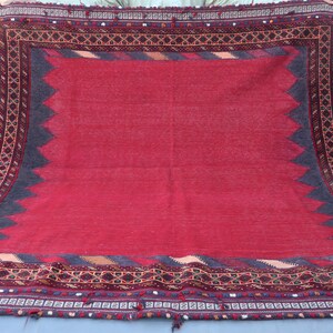 May include: A large, rectangular rug with a vibrant red central field. The rug features a dark gray border with a zigzag pattern and intricate geometric designs in brown, gold, and other colors. Tassels are visible at the bottom.