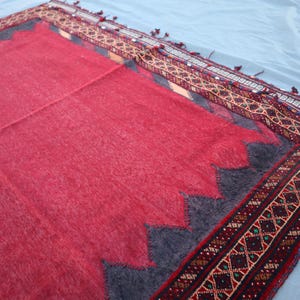 May include: A red rug with a dark gray zig-zag border and a patterned border in shades of red, brown, and green. The rug has a soft, textured appearance and is likely made of wool or a similar material. The rug is rectangular.