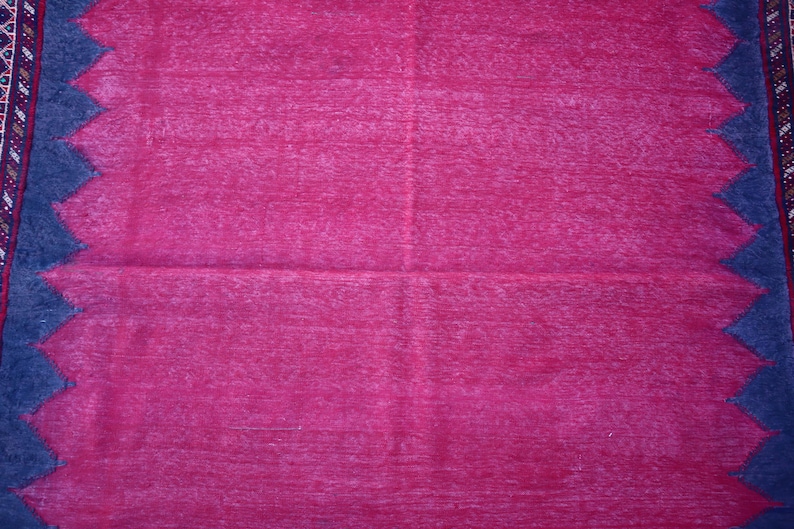 May include: A vibrant magenta rug with a textured surface. The rug features a dark blue zigzag border along the edges and a patterned border on one side. The rug is a home decor item.