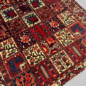 May include: A detailed close-up of a rectangular rug with a repeating pattern of squares. Each square features floral and geometric designs in red, navy blue, cream, and brown. The rug has a traditional, ornate style.