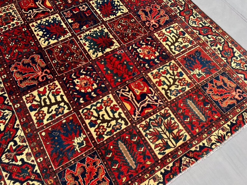 May include: A detailed close-up of a rectangular rug with a repeating pattern of squares. Each square features floral and geometric designs in red, navy blue, cream, and brown. The rug has a traditional, ornate style.