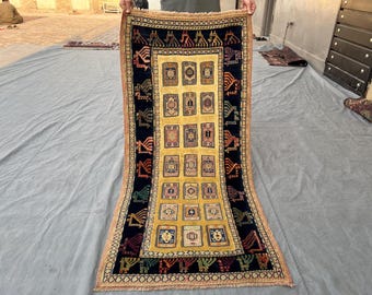 May include: Rectangular rug with a central yellow field featuring a series of framed designs. The rug has a dark blue border with repeating geometric and stylized bird motifs. The edges are trimmed with a fringed border in shades of orange and tan.