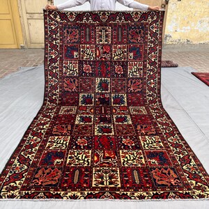 May include: A large, rectangular rug with a complex geometric pattern. The rug features a deep red background with repeating squares filled with floral and abstract designs in shades of blue, cream, and brown. The border has a detailed pattern.