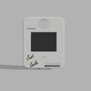 May include: A light grey, rectangular device with a black screen and the words "Just Smile" in cursive. The device has a circular opening at the top and a rectangular slot at the bottom. The device is on a grey background.