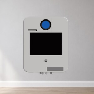 Puede incluir: Un dispositivo rectangular gris claro con esquinas redondeadas est&aacute; montado en una pared blanca. Cuenta con una pantalla negra, un elemento circular azul y una peque&ntilde;a secci&oacute;n rectangular. El dispositivo parece ser un producto tecnol&oacute;gico moderno.