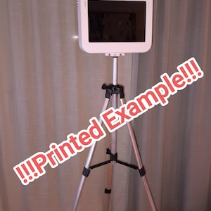 May include: A white photo booth on a silver tripod. The booth has a camera, screen, and a light. The text "!!!Printed Example!!!" is written across the image in red and white.
