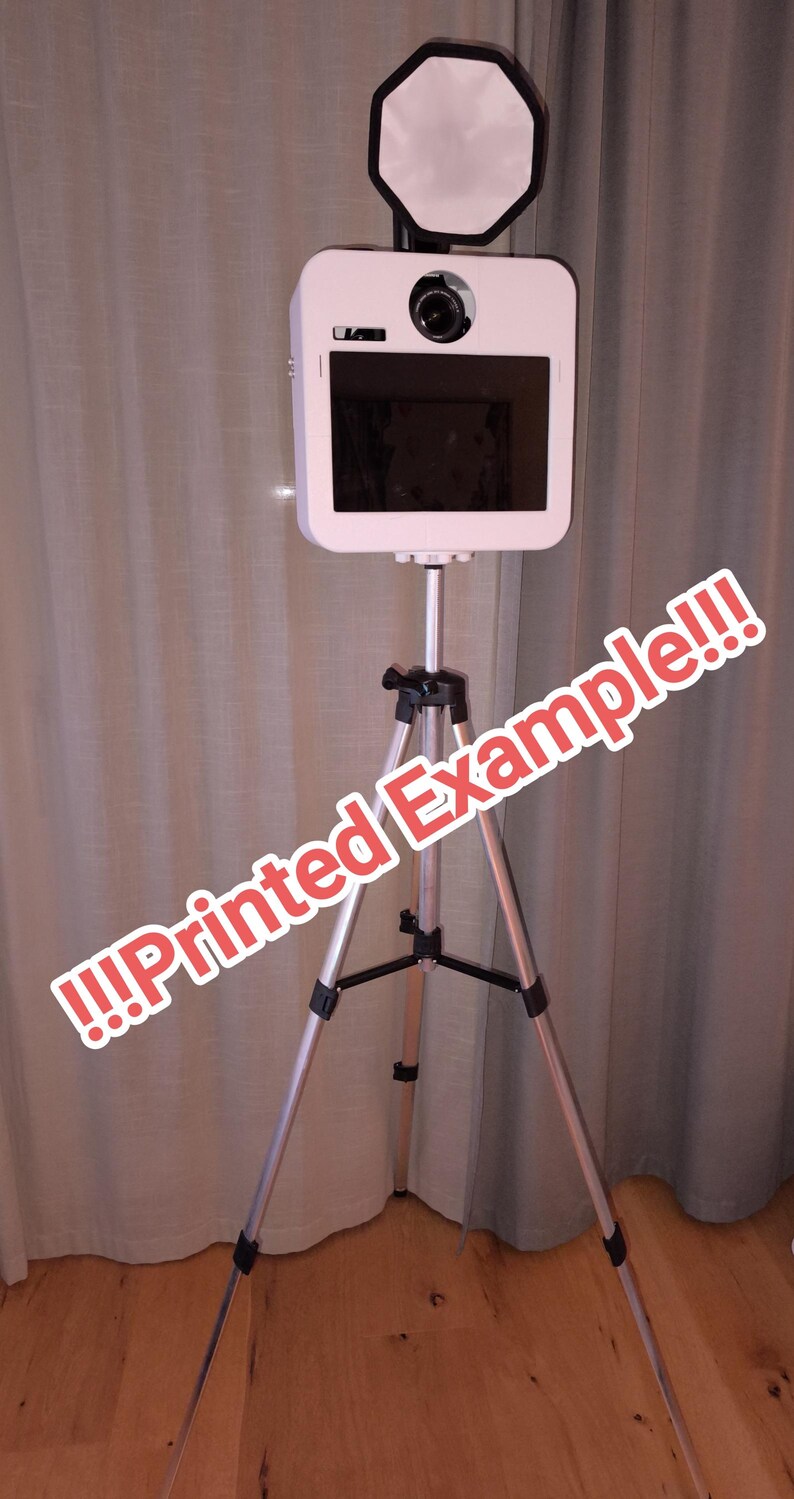 May include: A white photo booth on a silver tripod. The booth has a camera, screen, and a light. The text "!!!Printed Example!!!" is written across the image in red and white.