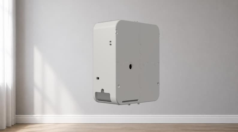 Puede incluir: Un dispositivo blanco rectangular con esquinas redondeadas, montado en una pared gris claro. El dispositivo tiene una parte superior perforada, una abertura circular y una ranura rectangular en la parte inferior. El dispositivo est&aacute; flotando en el aire.