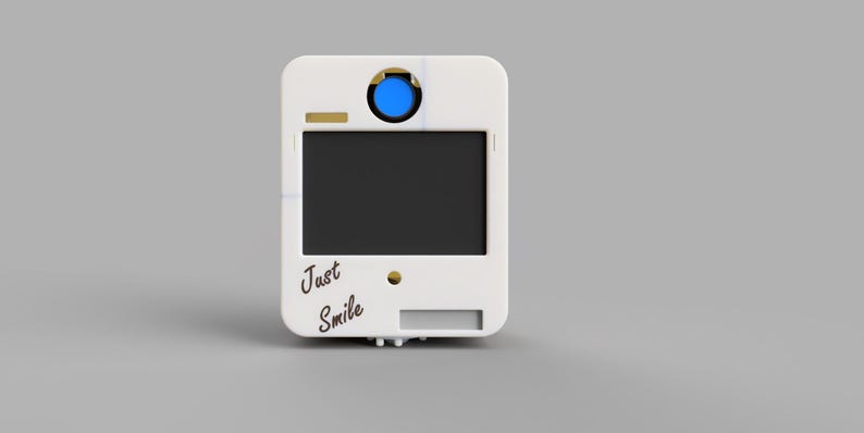 May include: A white photo booth with a black screen and the words "Just Smile" in cursive. It has a blue button and gold accents. The photo booth is rectangular with rounded corners.