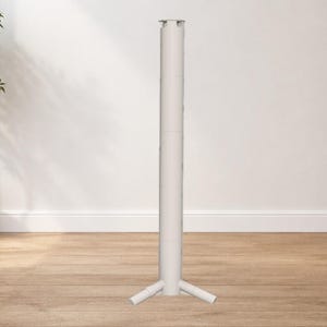 May include: A white, cylindrical stand with a three-legged base. The stand is made of metal and is designed to support a table or other object. The background includes a potted plant and a wooden floor. The stand's height is approximately 150 cm.