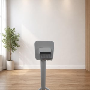 May include: A grey information stand with a rectangular top and a three-legged base. The stand is in a room with a wooden floor, a white wall, and a potted plant. The stand is made of metal.