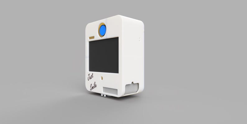 May include: A white photo booth with a black screen, a blue lens, and the words "Just Smile" in script. The booth has a rectangular shape with rounded edges and a small slot for photos.