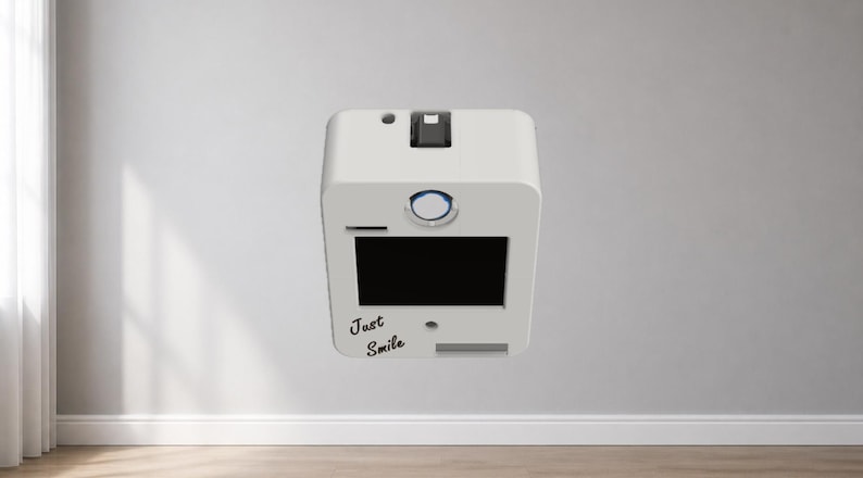 Puede incluir: Un dispositivo blanco y rectangular con una pantalla negra y las palabras "Just Smile" en cursiva. Tiene una ranura, un bot&oacute;n y una peque&ntilde;a abertura en la parte superior. El dispositivo est&aacute; montado en una pared blanca.