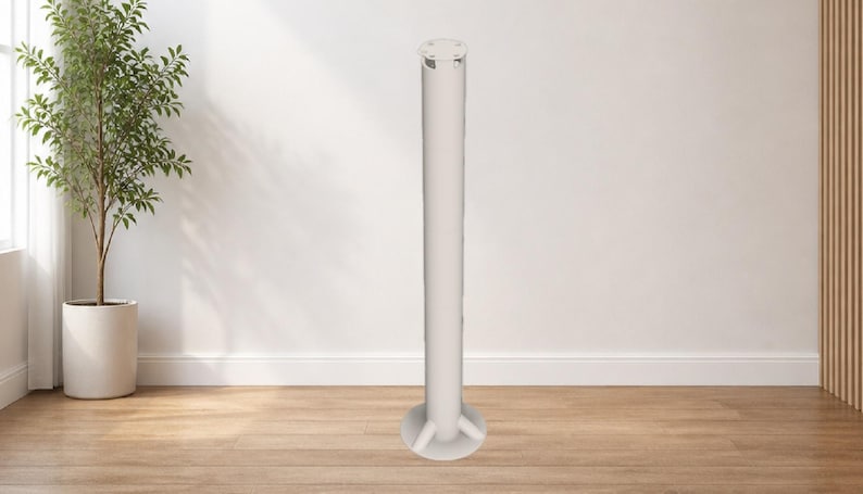 May include: A tall, white, cylindrical object with a circular base and a decorative top. The object stands on a wooden floor against a white wall. A potted plant is visible in the background.