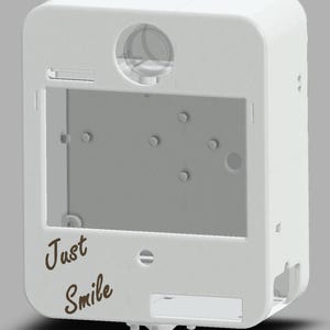May include: A white rectangular device with rounded corners, featuring a large rectangular opening and a circular lens. The words "Just Smile" are written in a brown, cursive font on the front. The device has several small holes and slots.