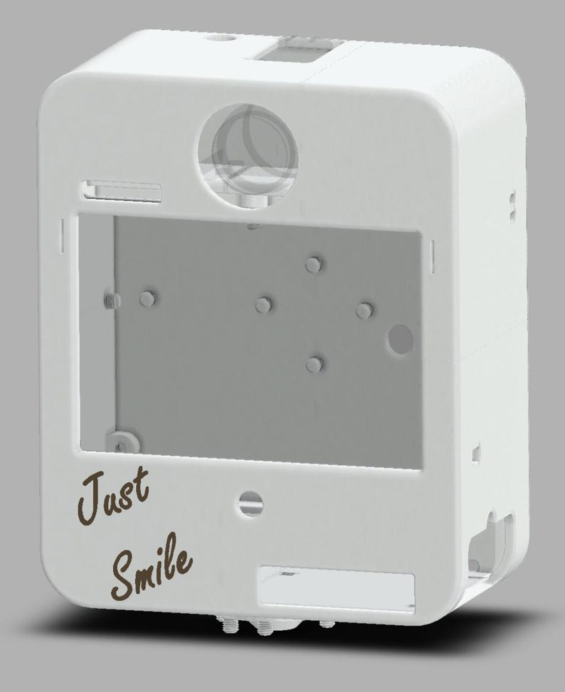 May include: A white rectangular device with rounded corners, featuring a large rectangular opening and a circular lens. The words "Just Smile" are written in a brown, cursive font on the front. The device has several small holes and slots.