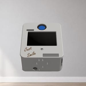 Puede incluir: Una cabina de fotos blanca y gris con una pantalla negra y un bot&oacute;n azul en la parte superior. Las palabras "Just Smile" est&aacute;n escritas en la parte delantera. La cabina tiene forma rectangular y flota en el aire.