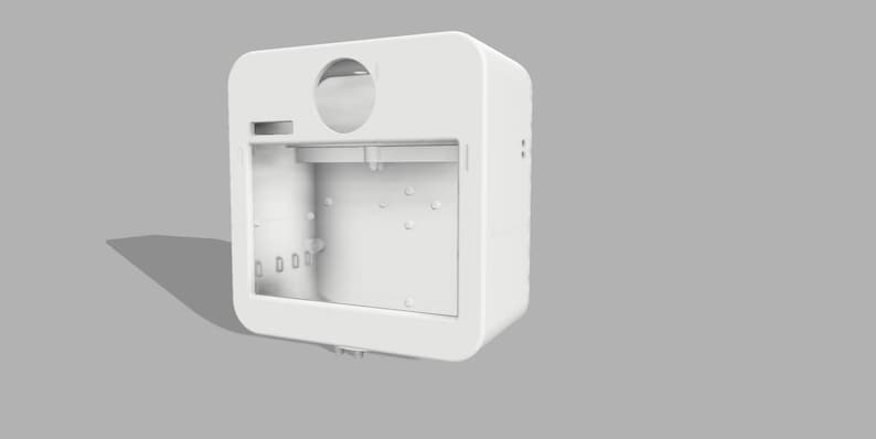 May include: A white, rectangular, open-faced device with rounded corners. It features a circular opening at the top, a rectangular slot, and several small circular indentations. The device is set against a gray background.